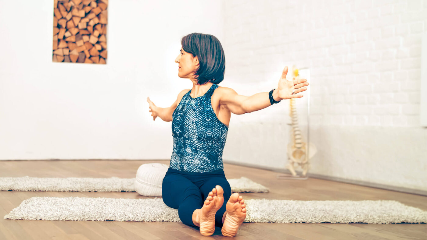 Maria doing the Pilates exercise Spine Twist, in the background a model of a spine